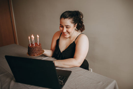 Une personne souriante tient une bougie d'anniversaire devant son téléphone pendant un appel vidéo